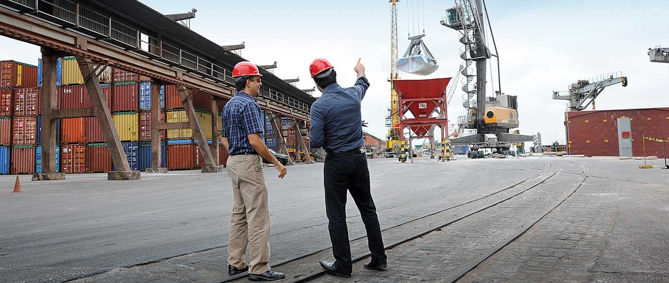 Two male workers in shipyard point at crane 
